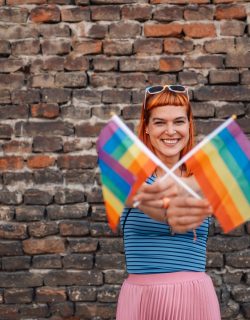 Young woman showing two lgbt flags with a brick wall background